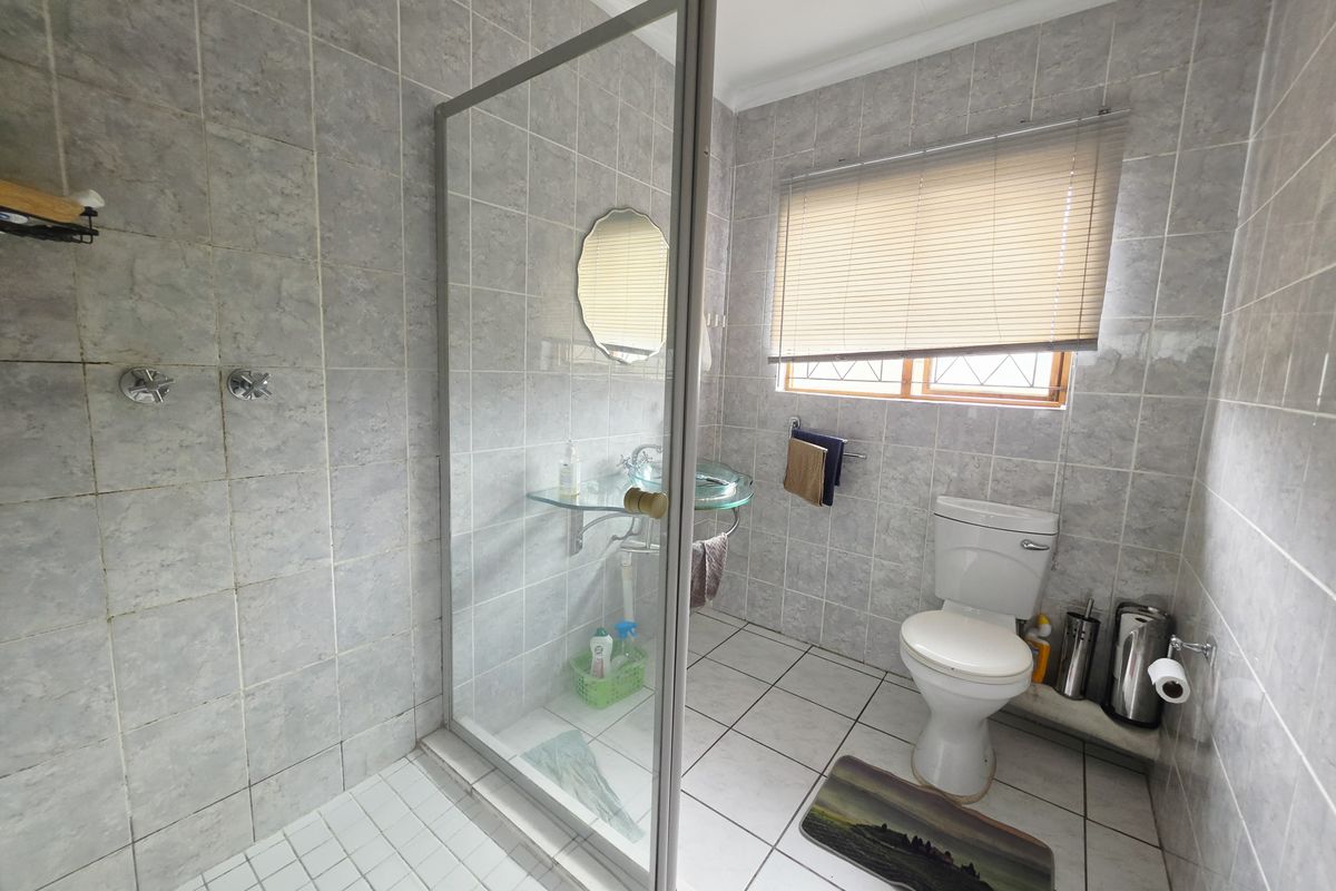 A functional bathroom featuring a glass-enclosed shower, wall-mounted basin, and toilet, finished with neutral wall and floor tiles.