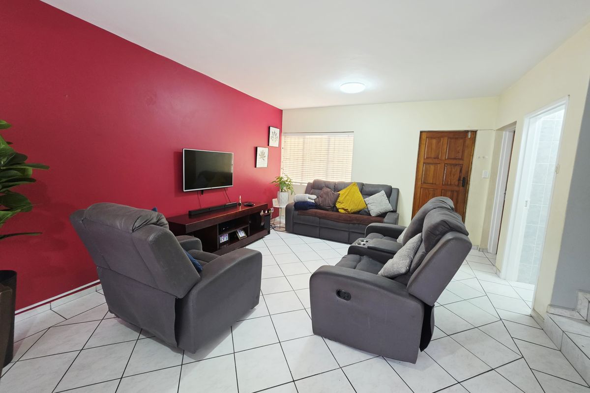 A living room featuring tiled flooring, a bold red accent wall, and a solid wood door leading to adjacent areas.