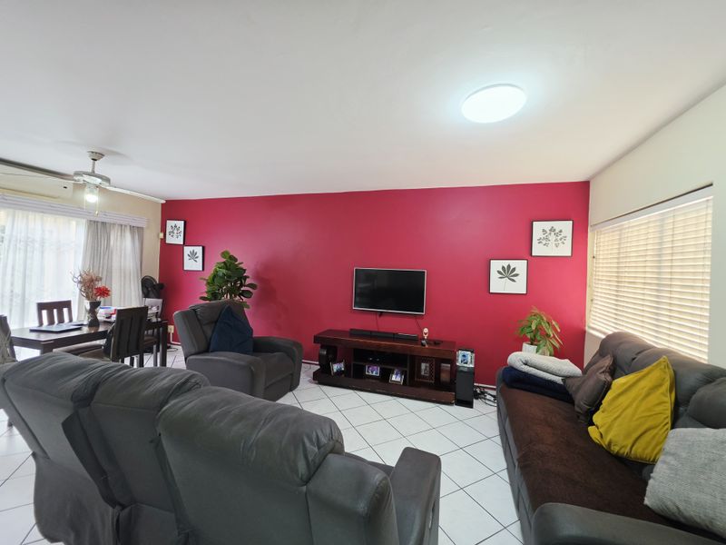 An open-plan living and dining area featuring tiled flooring, a ceiling fan, and large windows with fitted blinds.