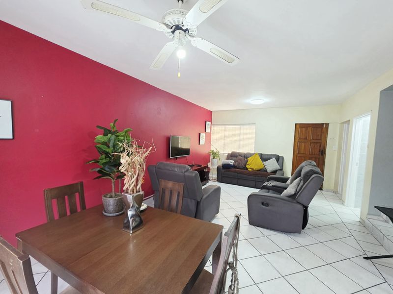 Open-plan living and dining area featuring tiled flooring, a ceiling fan, and a bold accent wall, providing a functional and versatile living space.