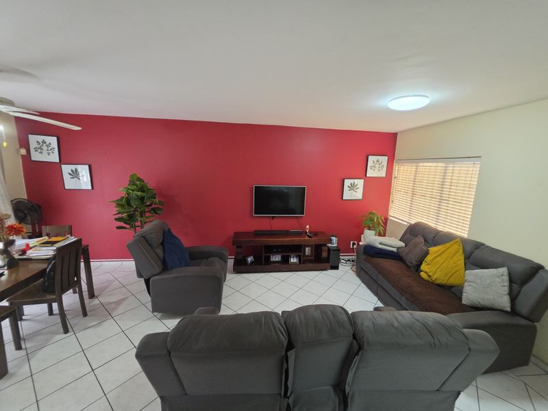 Open plan living area featuring tiled flooring, a ceiling fan, and a bold red accent wall with natural light from the window.