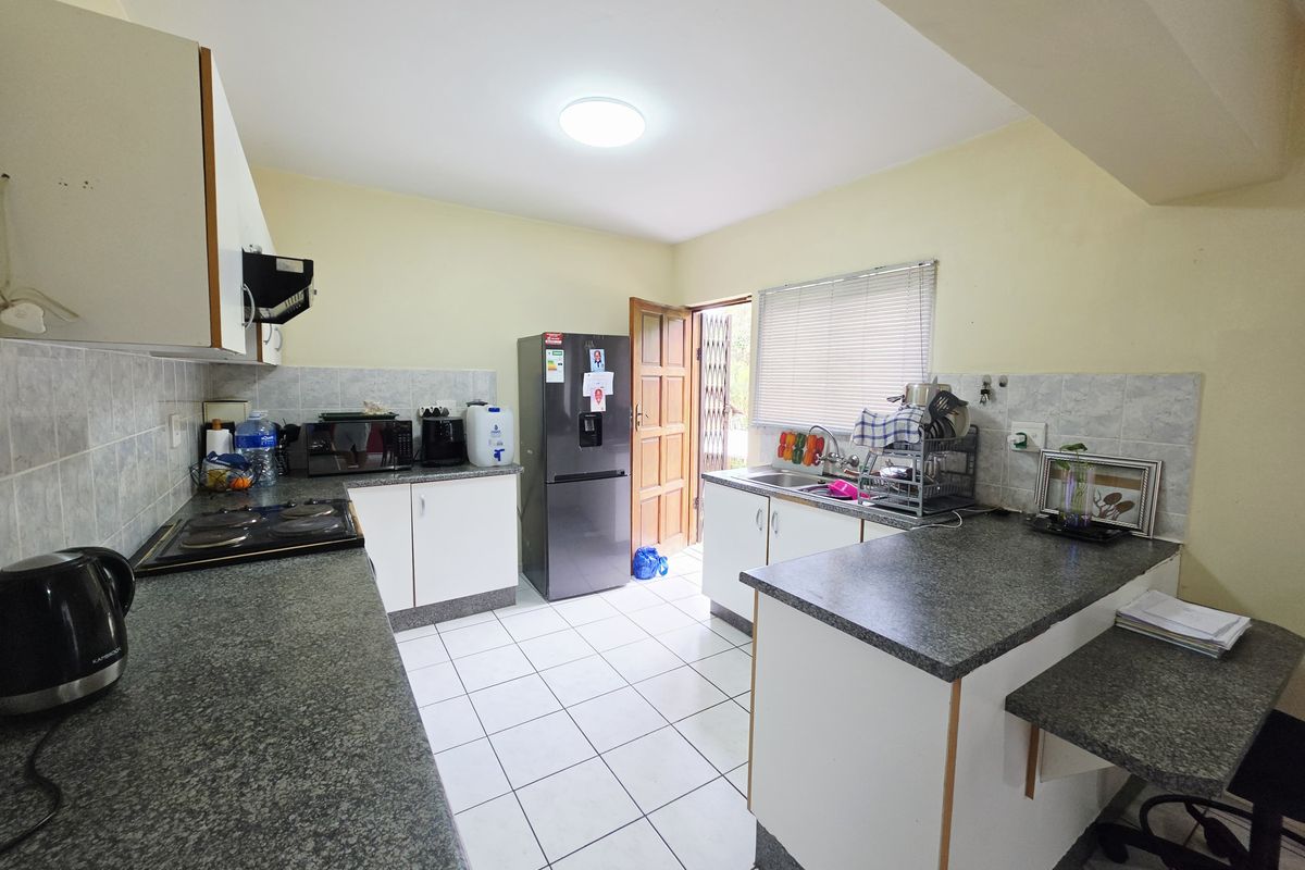Functional kitchen featuring granite countertops, tiled flooring, built-in cabinetry, and an electric hob with an extractor fan, offering direct access to the exterior.