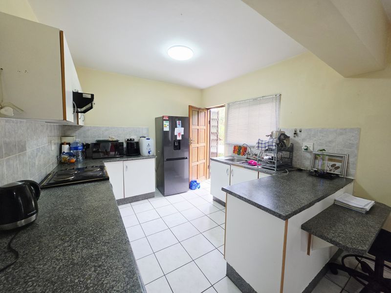 Functional kitchen featuring granite countertops, tiled flooring, built-in cabinetry, and an electric hob with an extractor fan, offering direct access to the exterior.