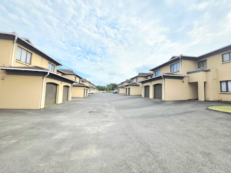 A wide-angle view of a townhouse complex driveway featuring multiple units with roller garage doors and paved access.
