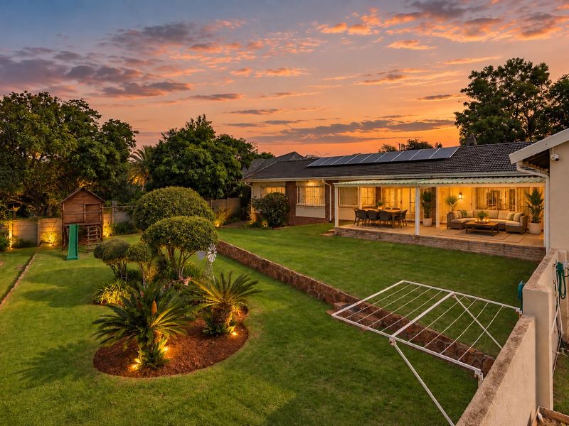 Spacious rear garden featuring a well-maintained lawn, landscaped beds, and a covered patio area with solar panels installed on the roof.