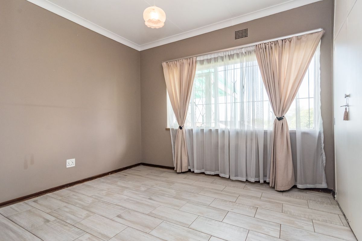 A clean, empty bedroom featuring light-toned tiled flooring, neutral wall paint, and a built-in cupboard with security bars on the window.