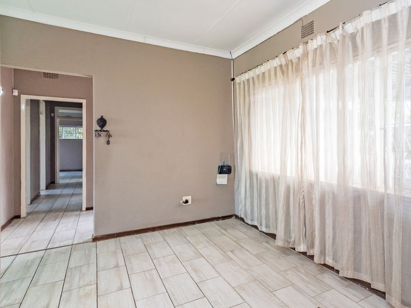 An empty living room featuring neutral wall tones, tiled flooring, and a large window with sheer curtains, providing a blank canvas for interior design.