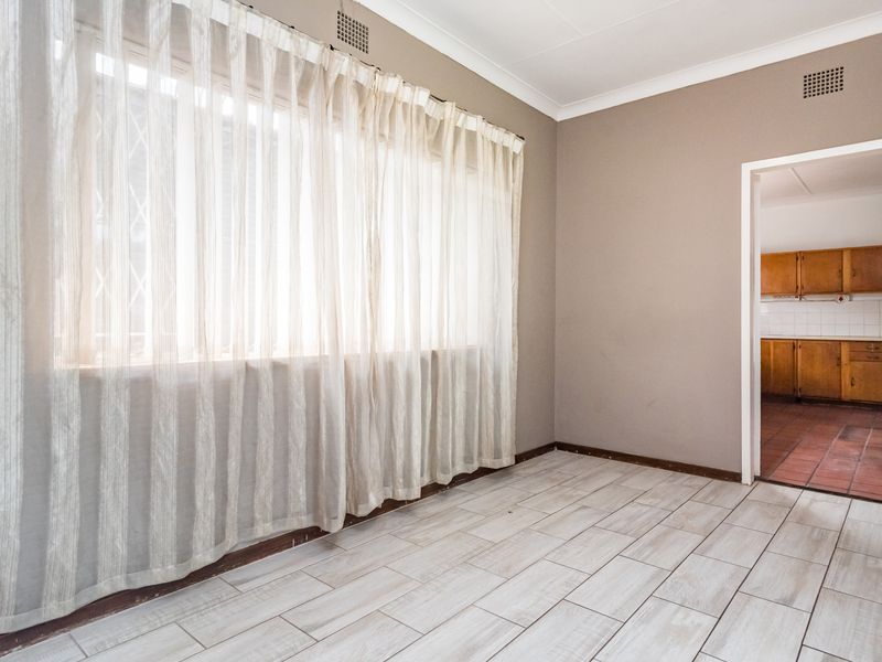 An empty living room featuring light-toned tiled flooring, coved ceilings, and a view through to the adjacent kitchen area.