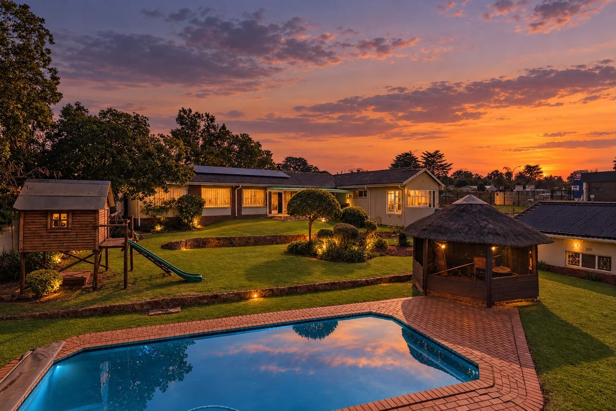 A beautifully landscaped rear garden featuring a swimming pool, brick-paved patio, thatched gazebo, and well-maintained lawn at sunset.