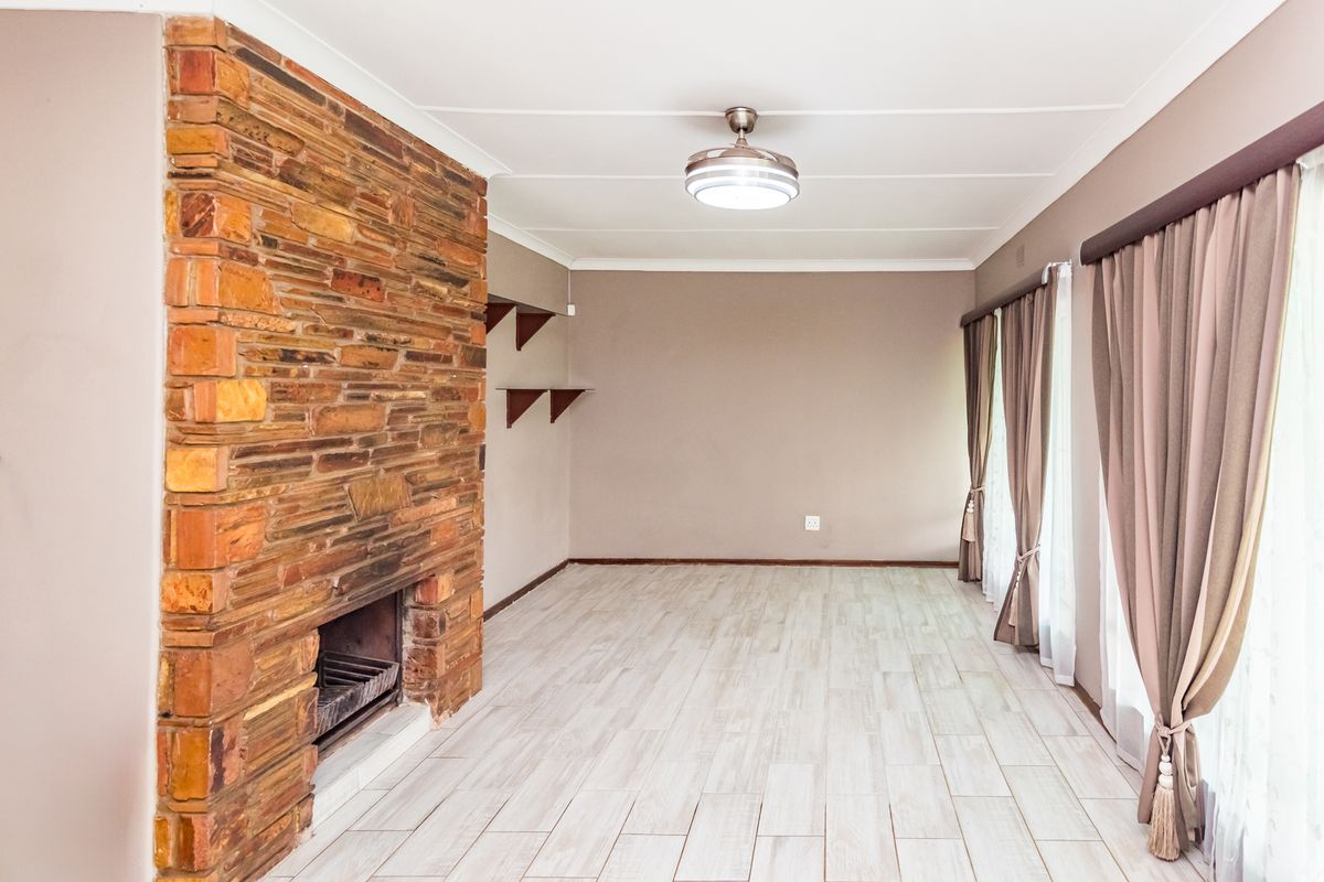 Spacious living room featuring a prominent stone fireplace, modern tiled flooring, and a ceiling fan, offering a clean and neutral canvas for interior design.
