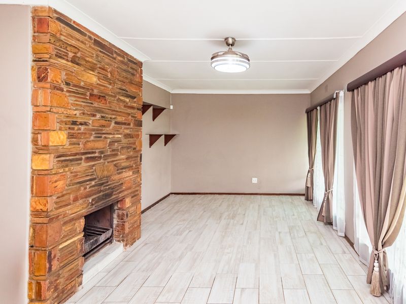 Spacious living room featuring a prominent stone fireplace, modern tiled flooring, and a ceiling fan, offering a clean and neutral canvas for interior design.