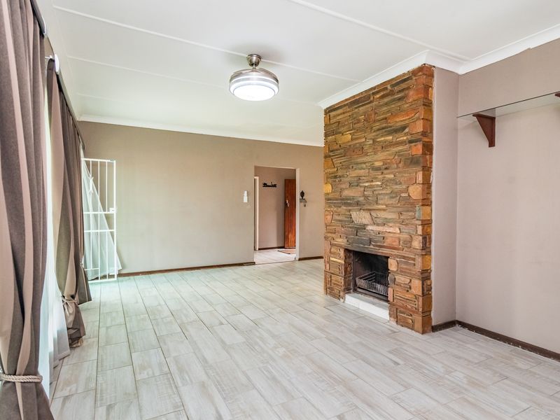 Spacious living room featuring a prominent stone fireplace, light-toned tiled flooring, and a ceiling fan, offering a neutral canvas for interior design.
