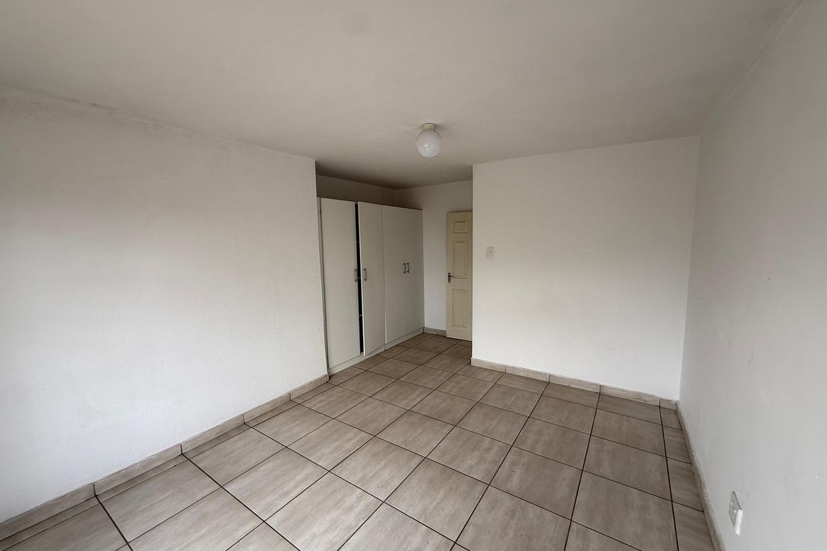 An empty bedroom featuring neutral tiled flooring and built-in storage cupboards, offering a blank canvas for personalization.