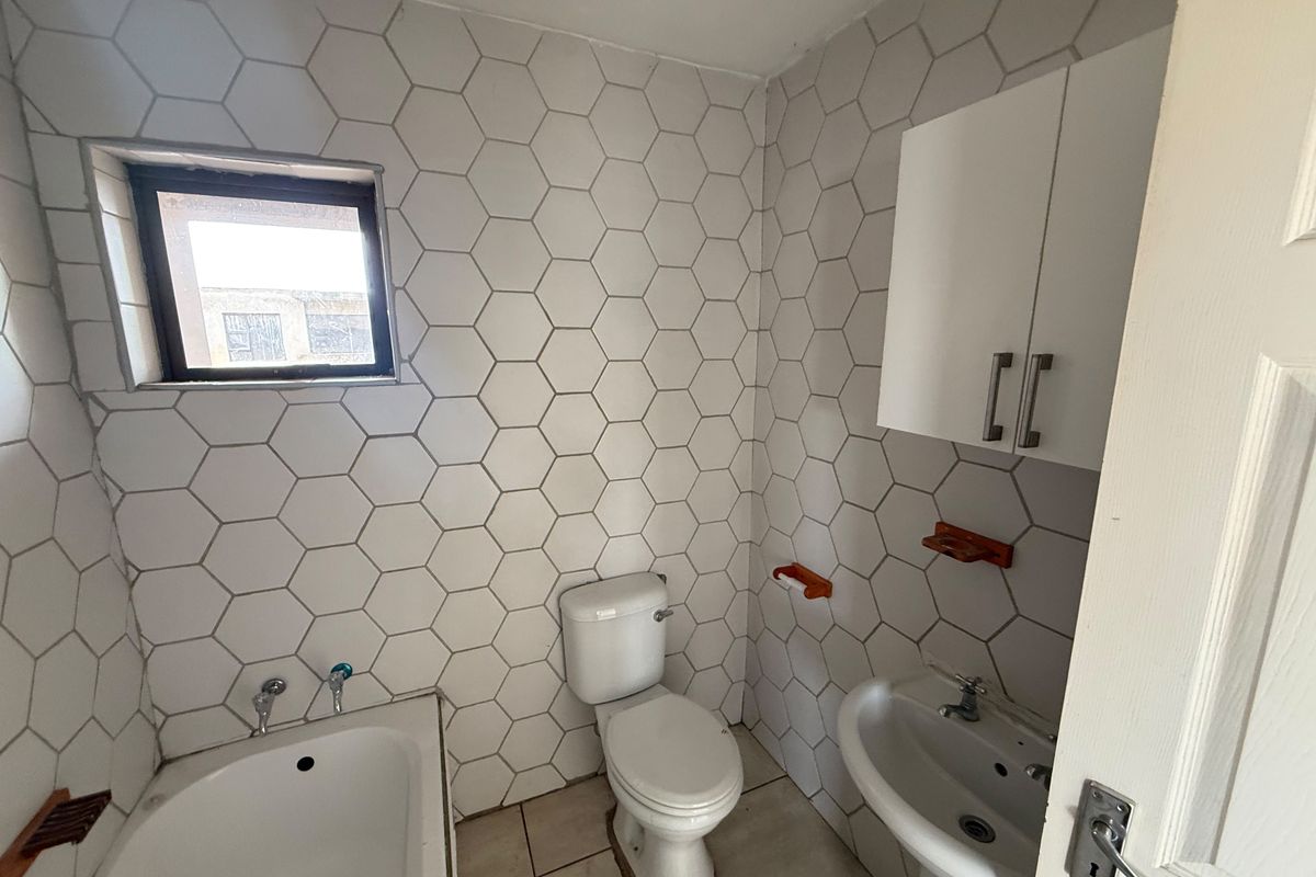 A functional bathroom featuring hexagonal wall tiling, a standard bathtub, pedestal basin, and wall-mounted storage cabinet.