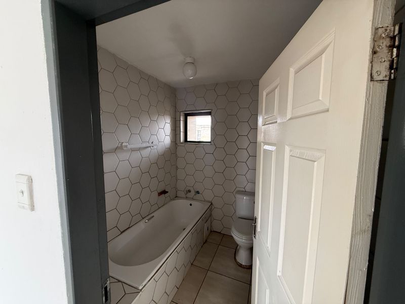 A compact bathroom featuring a bathtub, toilet, and modern hexagonal wall tiling, offering a functional space with potential for cosmetic updates.