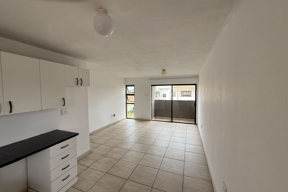 An empty open-plan living and kitchen area featuring tiled flooring, built-in cabinetry, and a sliding glass door leading to a balcony.