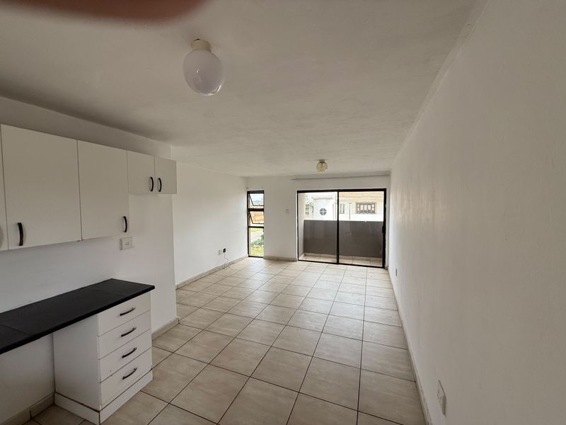 An empty open-plan living and kitchen area featuring tiled flooring, built-in cabinetry, and a sliding glass door leading to a balcony.