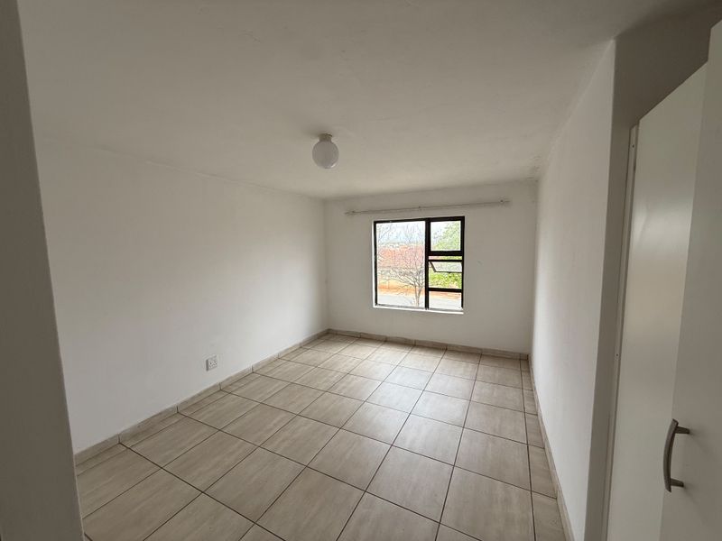 A clean, empty bedroom featuring neutral tiled flooring, a built-in cupboard, and a window providing natural light.