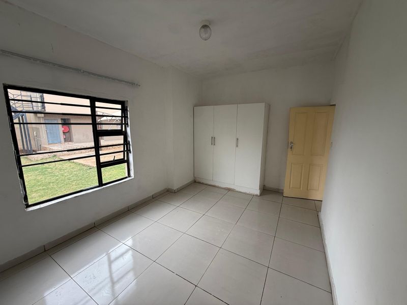 A vacant bedroom featuring tiled flooring, a built-in wardrobe, and a window with security bars, offering a clean and neutral space.