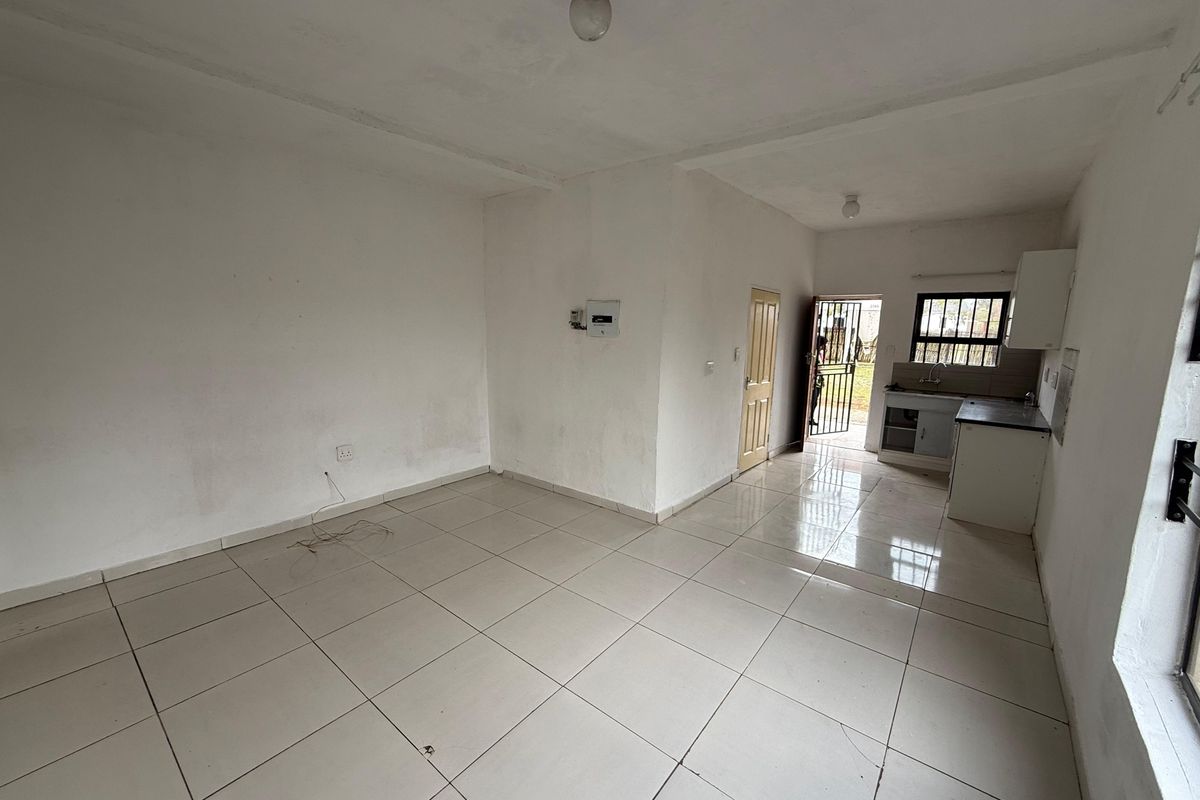An empty open-plan living and kitchen area featuring tiled flooring, basic cabinetry, and direct access to an exterior security gate.