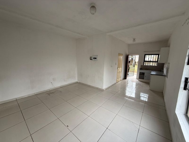 An empty open-plan living and kitchen area featuring tiled flooring, basic cabinetry, and direct access to an exterior security gate.