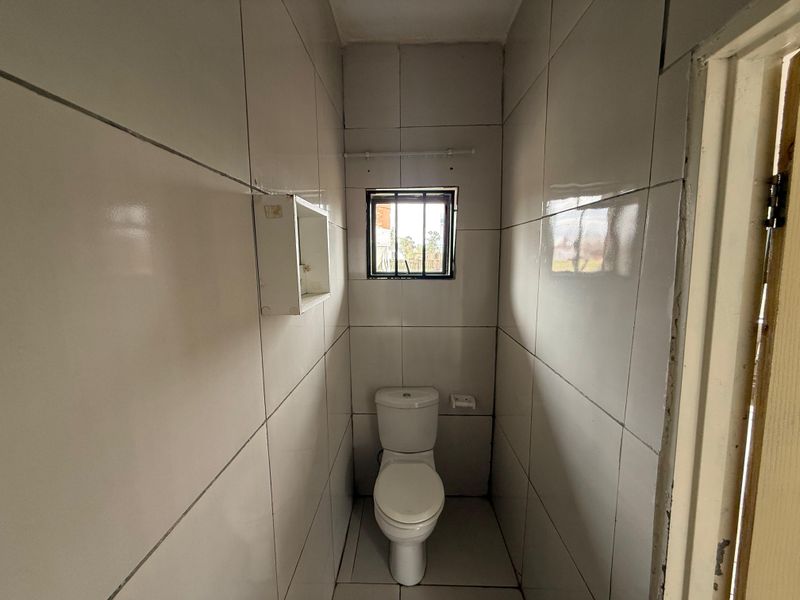 A compact, fully tiled guest toilet featuring a standard white toilet suite, a small window with security bars, and a recessed wall storage niche.