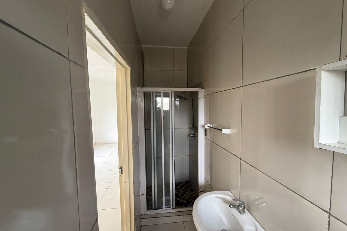 A compact bathroom featuring a shower enclosure and wall-mounted basin, finished with neutral wall and floor tiles.