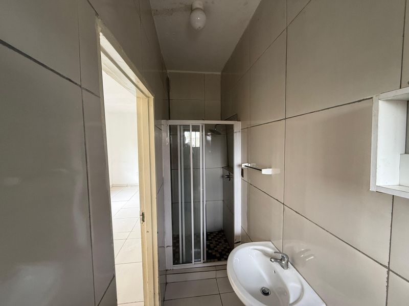 A compact bathroom featuring a shower enclosure and wall-mounted basin, finished with neutral wall and floor tiles.