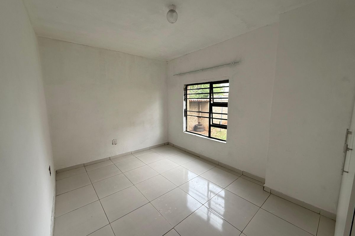 An empty bedroom featuring neutral tiled flooring, a window with security bars, and a curtain rail, providing a blank canvas for personalization.