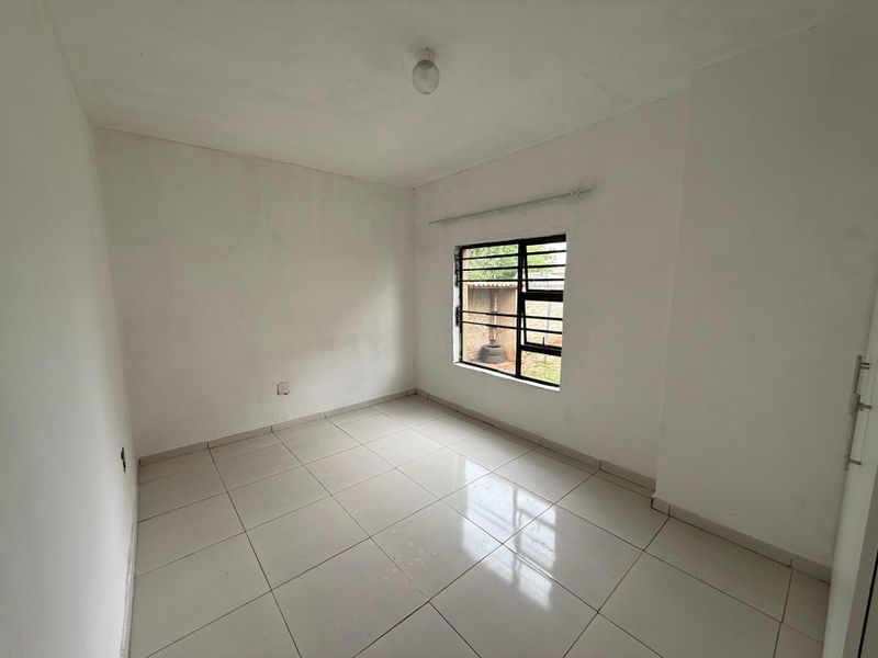 An empty bedroom featuring neutral tiled flooring, a window with security bars, and a curtain rail, providing a blank canvas for personalization.