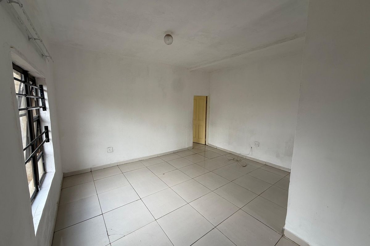 An empty, neutrally painted living area featuring tiled flooring and security bars on the window, providing a blank canvas for interior design.