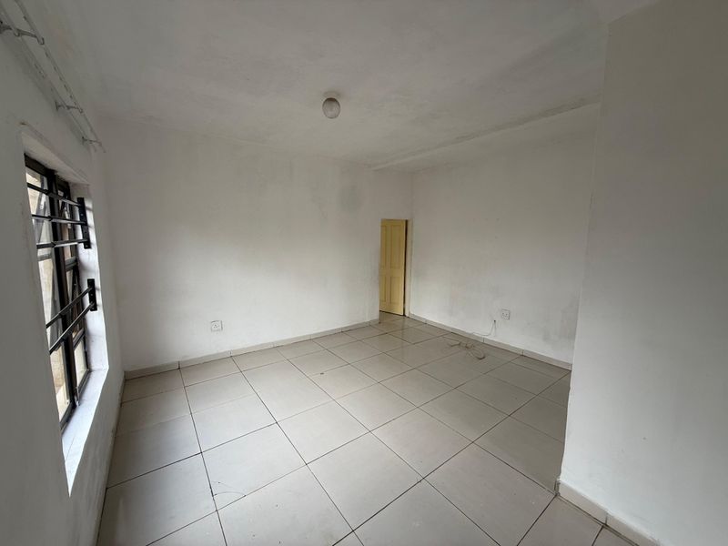 An empty, neutrally painted living area featuring tiled flooring and security bars on the window, providing a blank canvas for interior design.