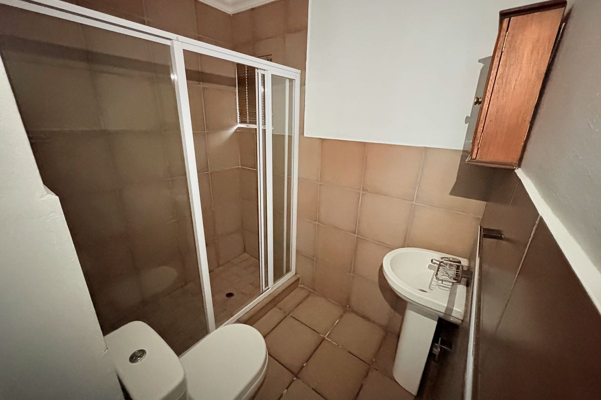 A compact bathroom featuring a shower enclosure, pedestal basin, and toilet, finished with neutral wall and floor tiling.