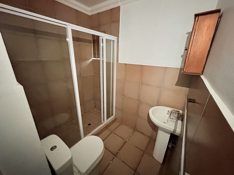 A compact bathroom featuring a shower enclosure, pedestal basin, and toilet, finished with neutral wall and floor tiling.