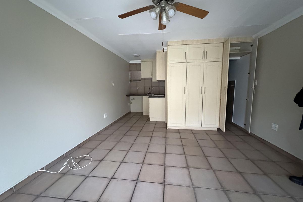 An open-plan living area featuring tiled flooring, a ceiling fan, and built-in kitchen cabinetry with integrated storage cupboards.
