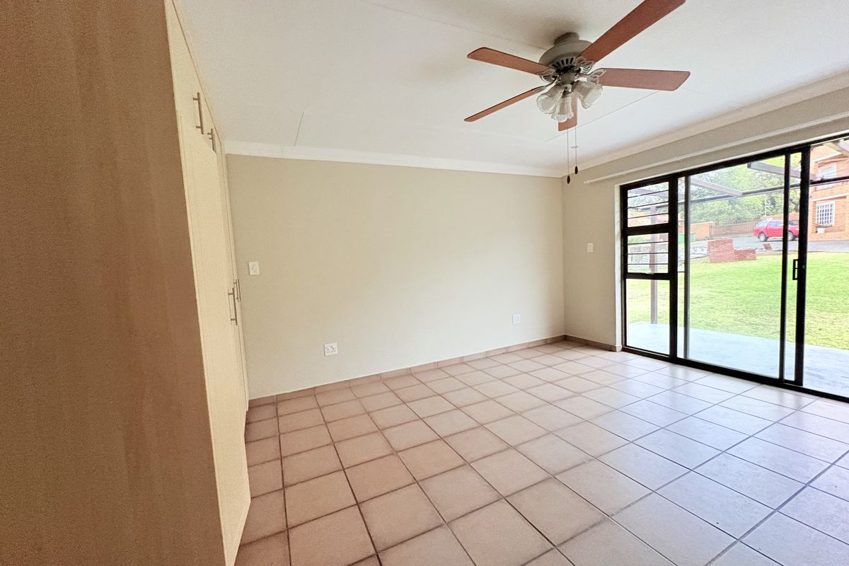 Spacious bedroom featuring built-in cupboards, tiled flooring, a ceiling fan, and a sliding glass door providing direct access to the garden.