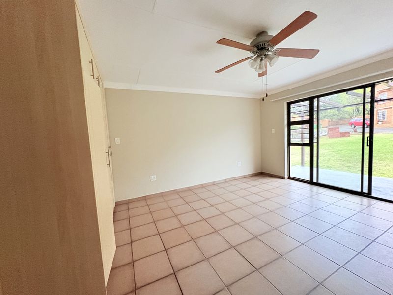 Spacious bedroom featuring built-in cupboards, tiled flooring, a ceiling fan, and a sliding glass door providing direct access to the garden.