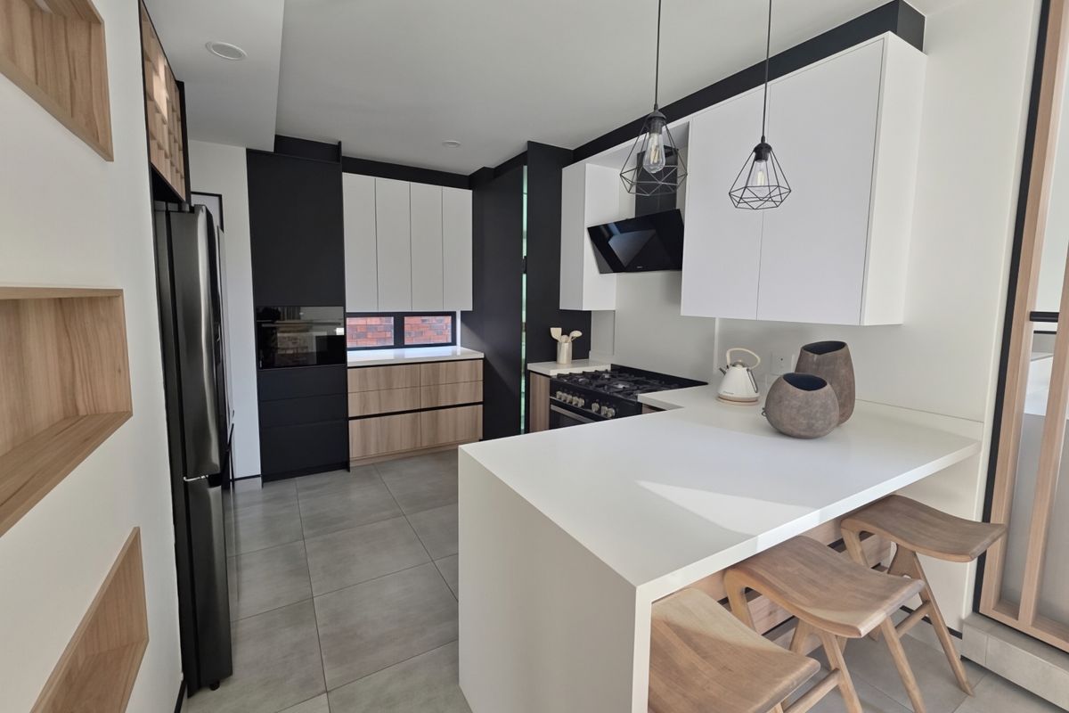 Modern kitchen featuring sleek two-tone cabinetry, quartz countertops, integrated appliances, and a breakfast bar with pendant lighting.