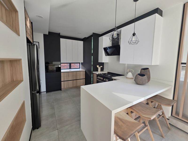 Modern kitchen featuring sleek two-tone cabinetry, quartz countertops, integrated appliances, and a breakfast bar with pendant lighting.