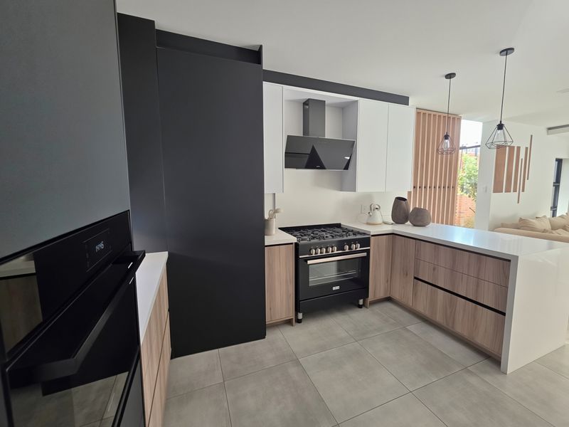 Modern kitchen featuring two-tone cabinetry, quartz countertops, a gas stove with extractor fan, built-in oven, and large format porcelain floor tiles.