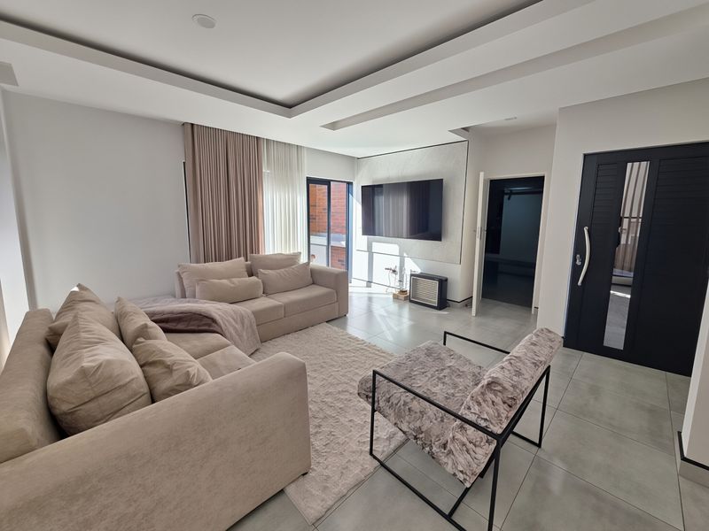 Modern living room featuring tiled flooring, a recessed ceiling design, and a sliding glass door providing natural light.