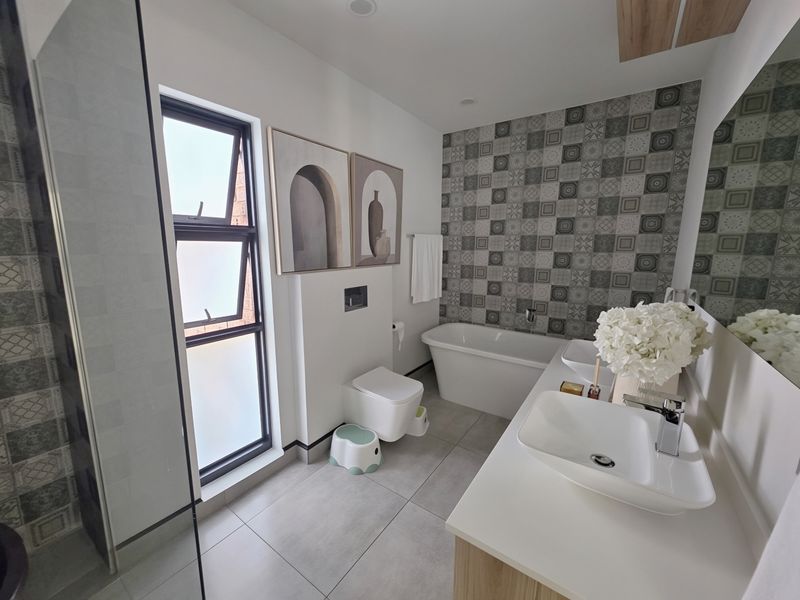 Modern bathroom featuring a freestanding bathtub, wall-hung toilet, double vanity with vessel sinks, and a stylish tiled feature wall.