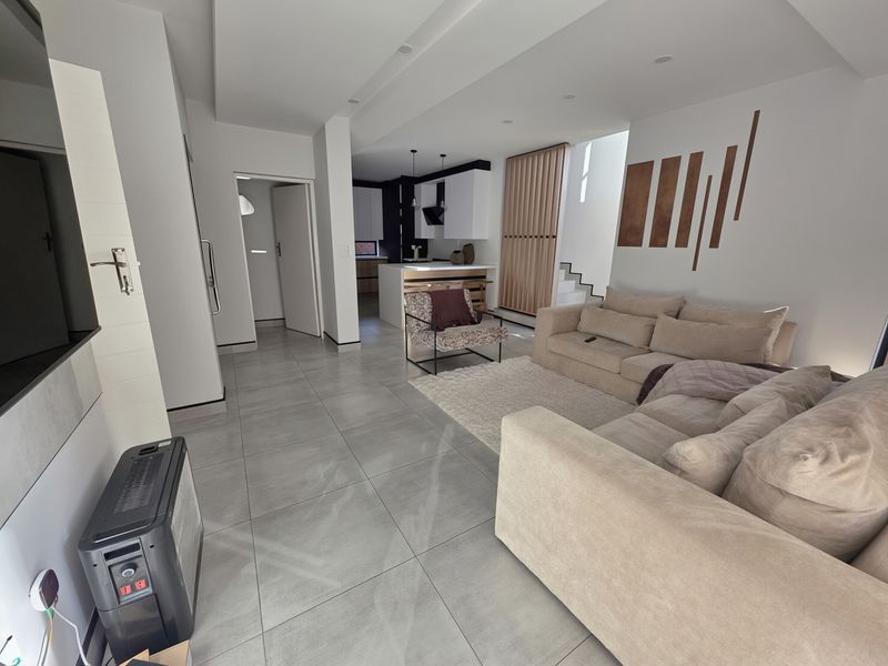 Modern open-plan living area featuring large format floor tiles, recessed lighting, and a contemporary kitchen with a central island and timber slat feature.