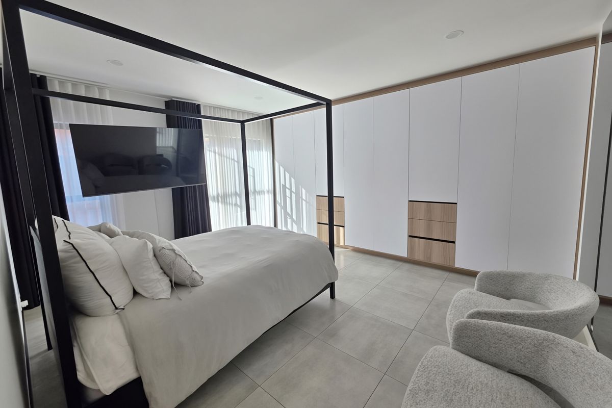 Modern bedroom featuring extensive built-in cabinetry with wood-accented drawers, large format floor tiles, and recessed ceiling lighting.