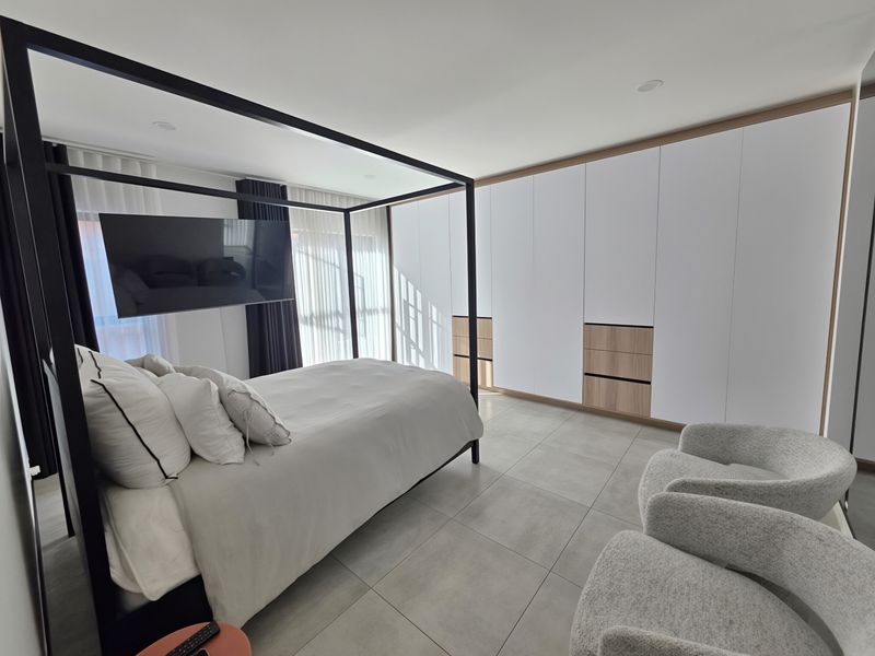 Modern bedroom featuring extensive built-in cabinetry with wood-accented drawers, large format floor tiles, and recessed ceiling lighting.