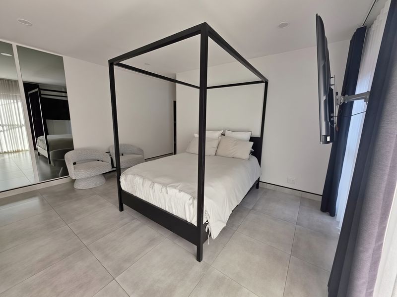 A modern, spacious bedroom featuring large-format floor tiles, recessed lighting, and extensive built-in mirrored wardrobes.