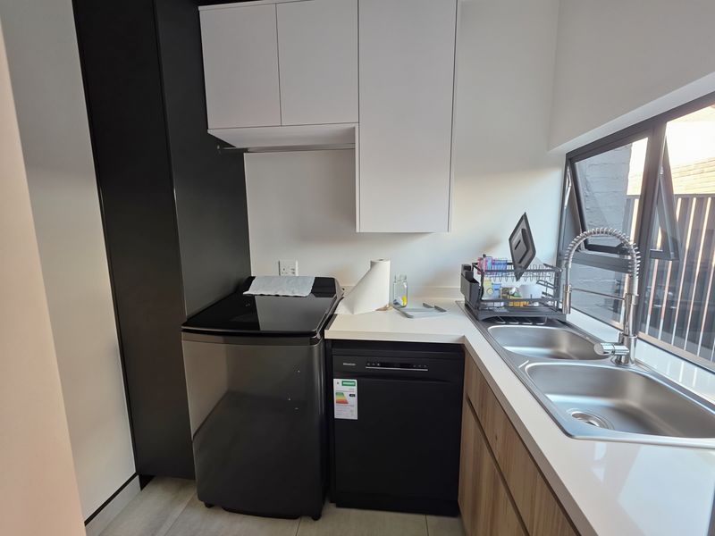 Modern scullery featuring sleek white and dark cabinetry, stone countertops, a double stainless steel sink with gooseneck tap, and integrated laundry and dishwashing appliances.