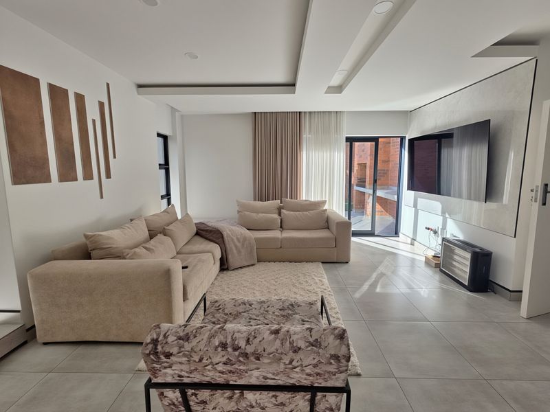 Modern living room featuring large format floor tiles, a recessed ceiling with downlights, and a feature wall with direct access to an outdoor patio area.