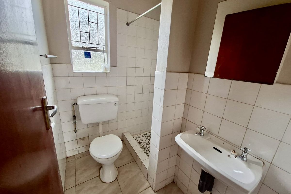 A compact, dated bathroom featuring a pedestal basin, toilet, and a tiled shower area with basic finishes.