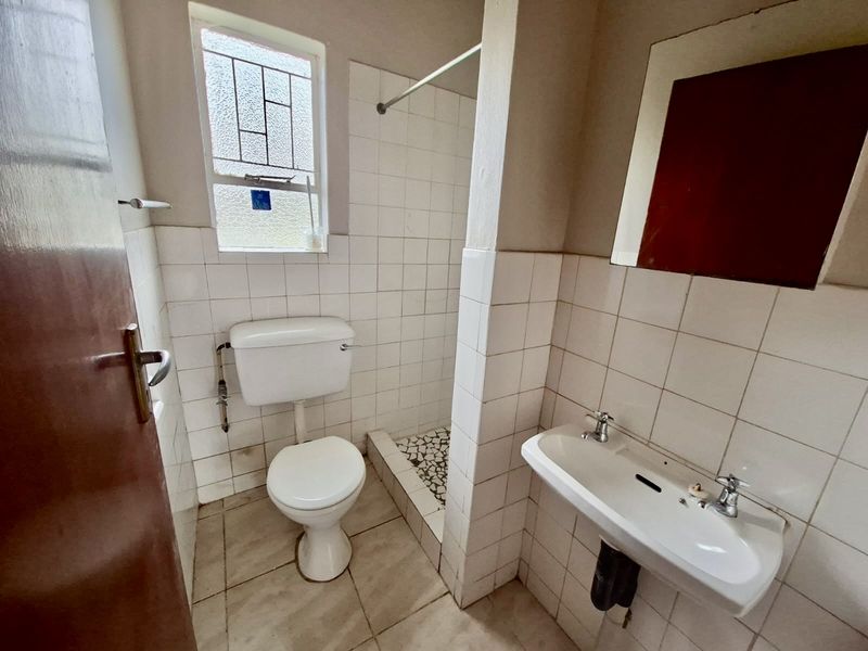 A compact, dated bathroom featuring a pedestal basin, toilet, and a tiled shower area with basic finishes.